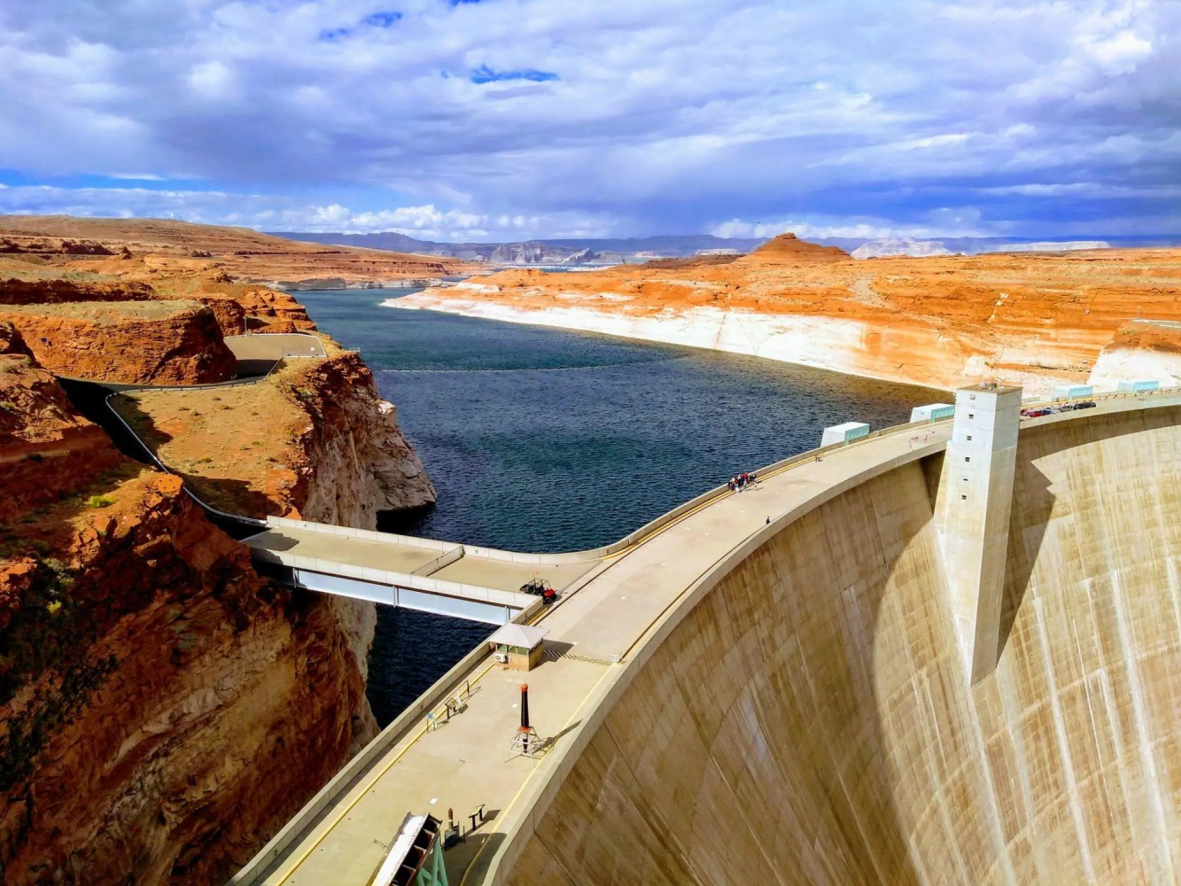 Aerial view of a large dam with a bridge, surrounded by red rock formations and a river.