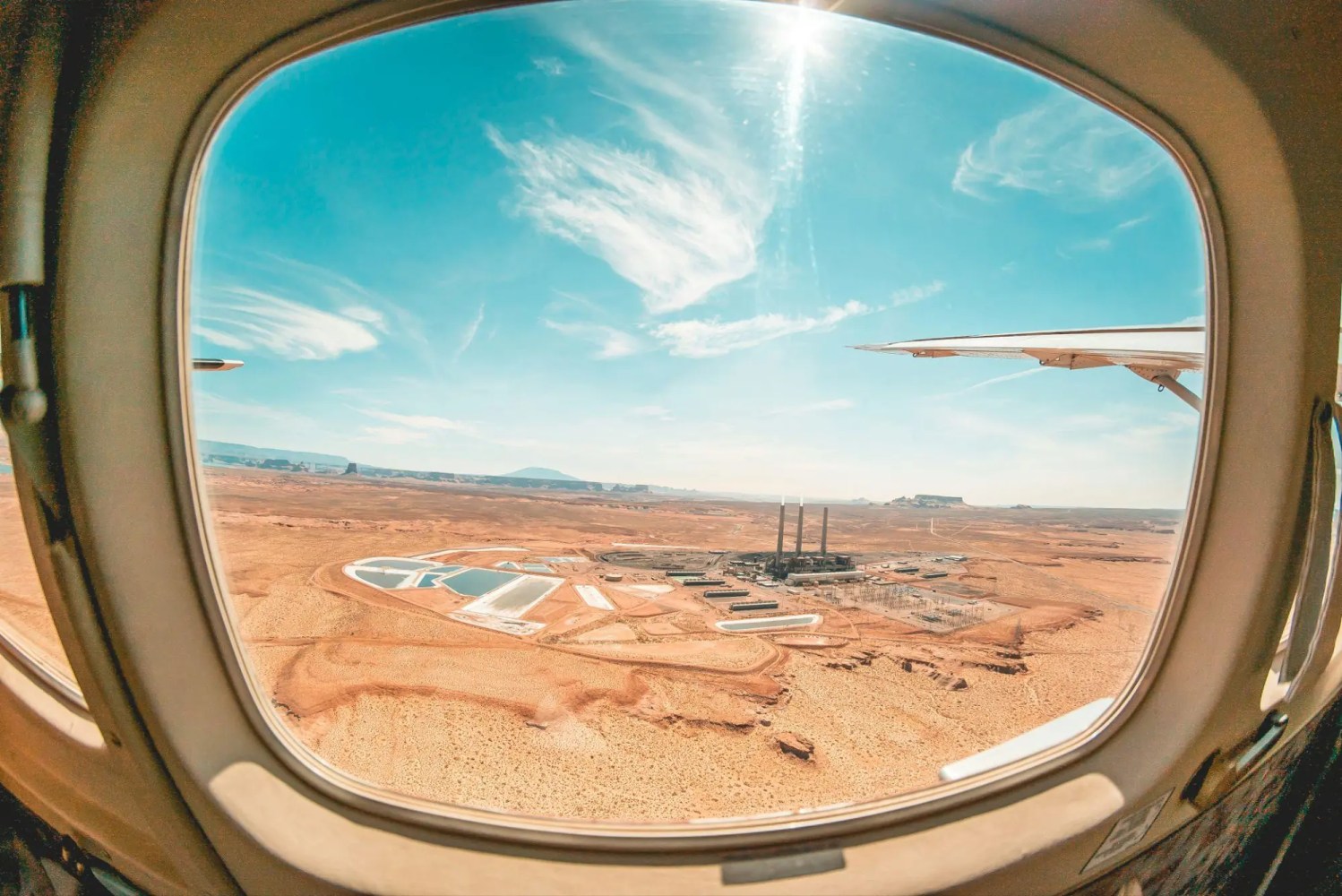 View from airplane window of desert landscape and power plant under a blue sky.