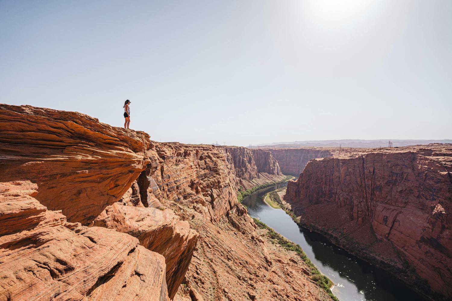 Person standing on canyon edge overlooking a river under a clear sky.