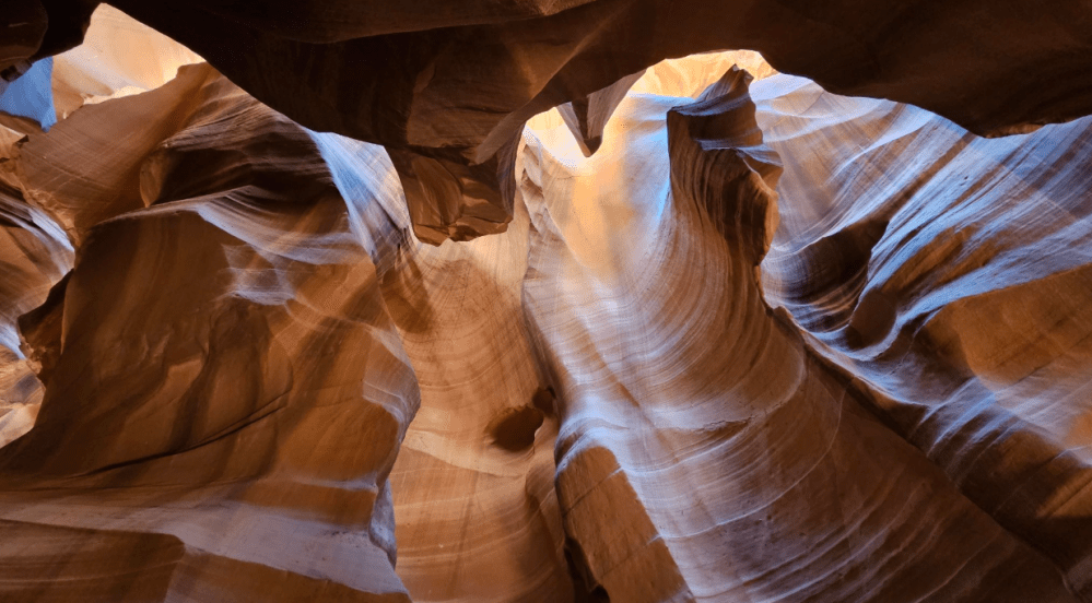 Curved sandstone walls with light streaming through a narrow canyon opening.