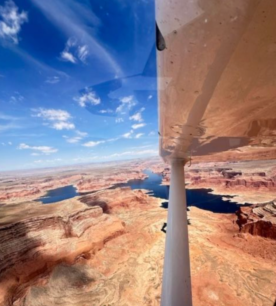 Aerial view of canyon with winding river under airplane wing, clear blue sky.