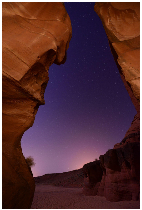 Narrow canyon with starry night sky and reddish rock walls.