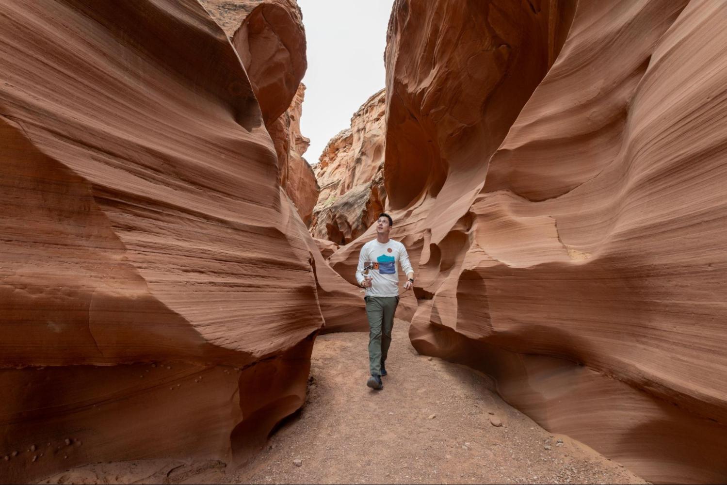 Person walking through a narrow, wavy red rock canyon.