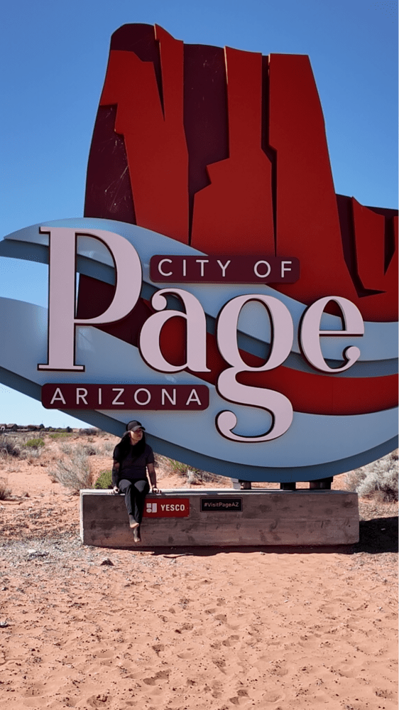 Person sitting by City of Page, Arizona sign in a desert landscape.