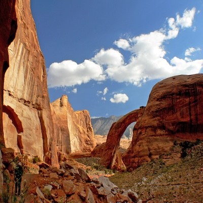 Natural sandstone arch in desert landscape with blue sky and clouds.
