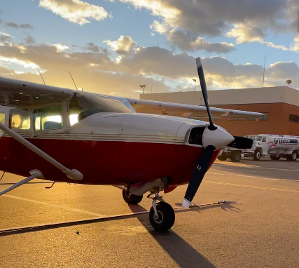 Small red airplane on tarmac at sunset, casting long shadows.