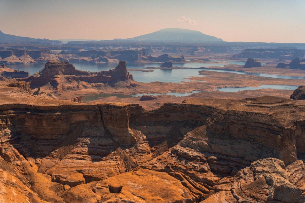 Vast canyon landscape with rocky cliffs and distant mountains under a clear sky.