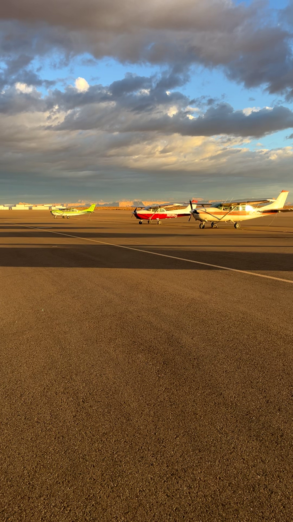 Small airplanes parked on an airport runway with a cloudy sky.